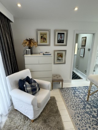 A comfortable white armchair.  Behind a wall featuring framed artwork.